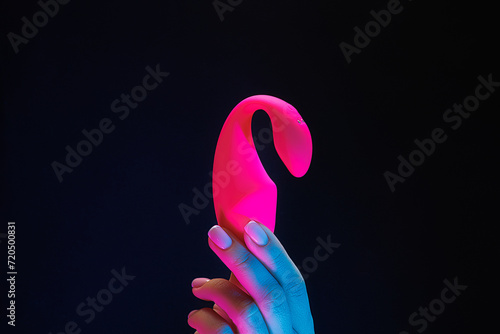 Close-up of a girl holding a red-colored sexual entertainment toy. Sex toy clitoral vibrator on a black background with neon lights. photo