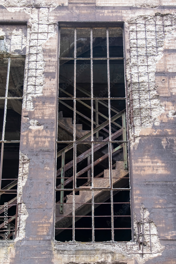 Low angle view of façade of a building in abandoned and dilapidated industrial steel mill in public Landschaftspark, Duisburg, Germany with large unglazed window and steel and concrete stairs
