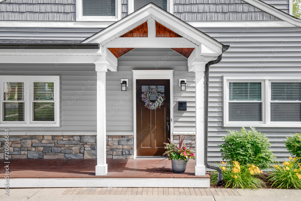 A grey modern farmhouse front door with a covered porch, wood front door with glass window, and grey vinyl and wood siding. A grey modern farmhouse front door with a covered porch, wood front door with glass window, and grey vinyl and wood siding.