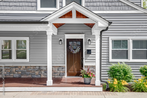 A grey modern farmhouse front door with a covered porch, wood front door with glass window, and grey vinyl and wood siding.