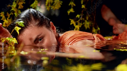 In the water, surrounded by yellow flowers and green branches, the girl attracts our attention with her magical attractiveness, transferring us to the inner world of harmony and beauty. photo