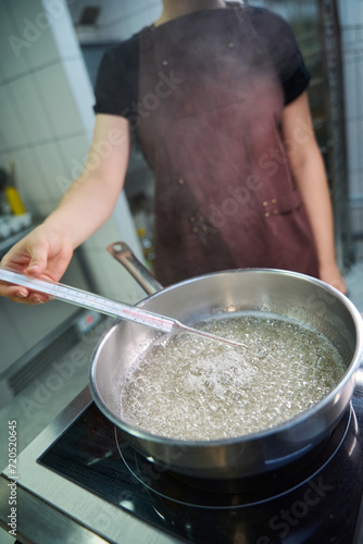 Qualified pastry chef checking temperature of sugar syrup during cooking