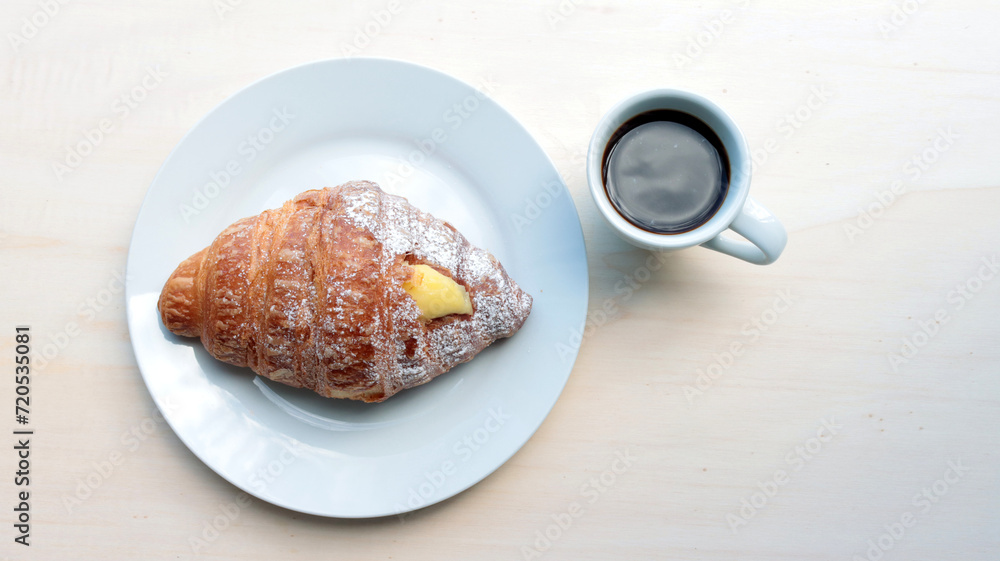 croissant stuffed with cream and cup of coffee on wooden table, natural light
