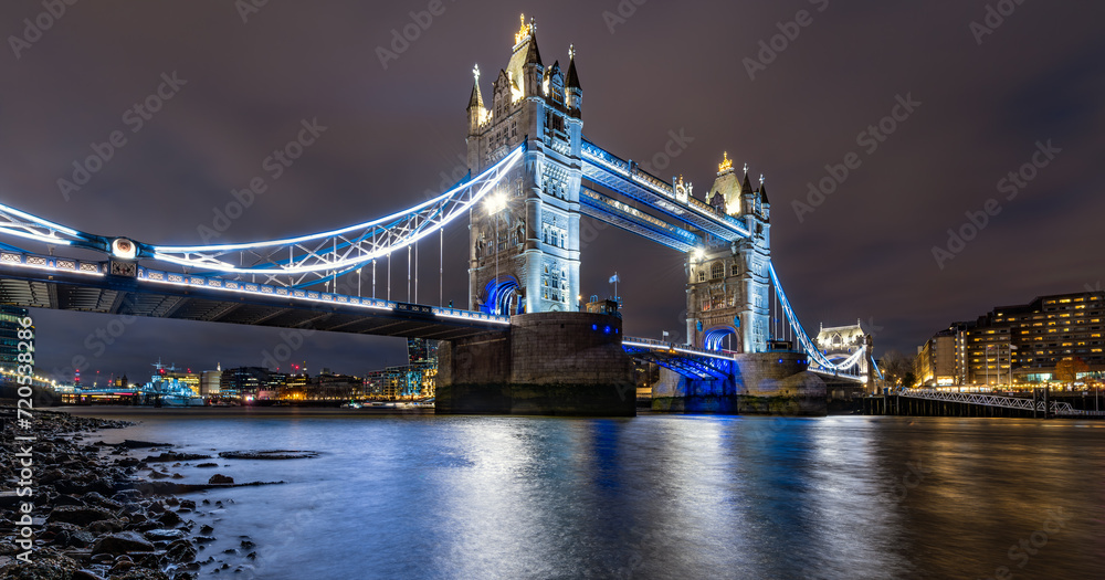 Tower Bridge night time panorama in London. Iconic landmark spanning over river Thames at with colorful illumination. Monument, sight and tourist attraction in british metropole from river bank.