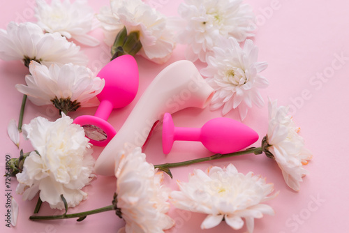 Concept erotic sex toy for female. Vacuum vibrator and butt plug on pink background with flowers, flat lay.
