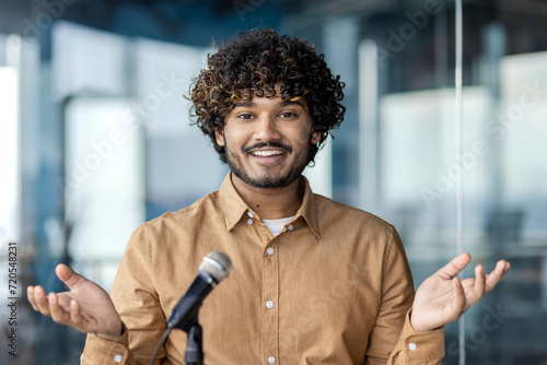 Εκτύπωση καμβά Handsome arab businessman sitting in stylish office and speaking in front of microphone