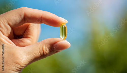 Female hand holding a small yellow capsule of nutritional supplement. Food supplement, vitamin D, omega, vitamin C, multivitamins. Soft focus
