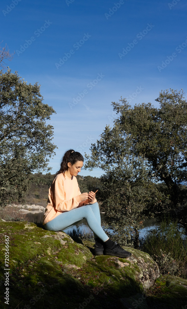 Woman sitting looking at cell phone in nature dressed in peach color