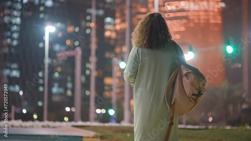 lonely woman walking in megapolis in night, back view of female townswoman against high skyscrapers photo