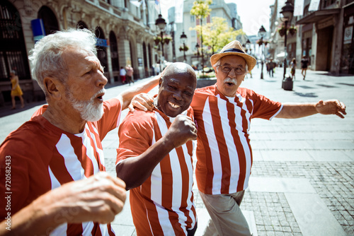 Senior friends celebrating and singing in matching striped shirts on city street photo
