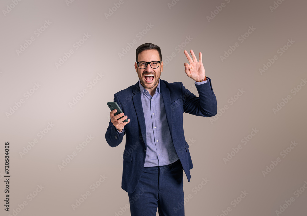 Young businessman with smart phone screaming ecstatically and gesturing OK sign on white background Young businessman with smart phone screaming ecstatically and gesturing OK sign on white background
