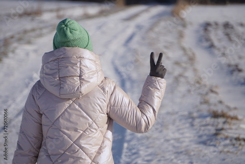 Kobieta pokazuje gest Victorii. Symbol „V” widoczny z tyłu. Słoneczna pogoda w czasie zimy.