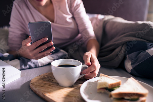 Woman using smartphone while having breakfast in bed