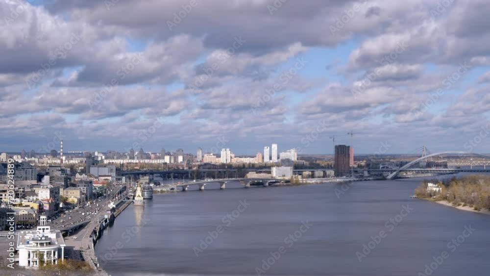 Panoramic View of Kyiv, the Dnieper River, Sleeping Areas, Podolsky Bridge. View from the glass bridge to the green island, metropolis. Cloud landscape, green trees. Kyiv is the capital of Ukraine. Panoramic View of Kyiv, the Dnieper River, Sleeping Areas, Podolsky Bridge. View from the glass bridge to the green island, metropolis. Cloud landscape, green trees. Kyiv is the capital of Ukraine.