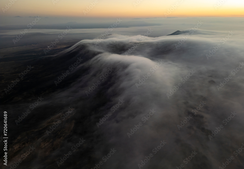Soft clouds cascade over the darkened landscape of Fuerteventura as the first light of sunrise peeks over the horizon Soft clouds cascade over the darkened landscape of Fuerteventura as the first light of sunrise peeks over the horizon