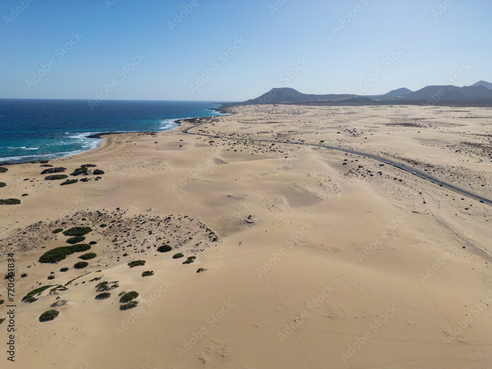 Expansive view of the Corralejo Dunes meeting the blue sea with mountainous backdrop in Fuerteventura Expansive view of the Corralejo Dunes meeting the blue sea with mountainous backdrop in Fuerteventura