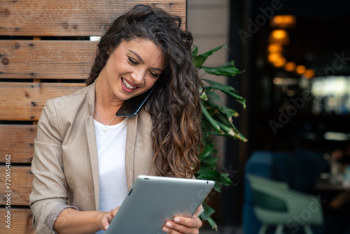Smiling young beautiful business woman talking on a mobile phone while using fintech technology device. © Dorde