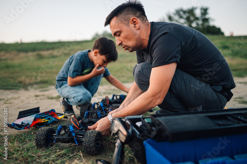 Father and his son fixing toy cars after fun racing time, outdoors.