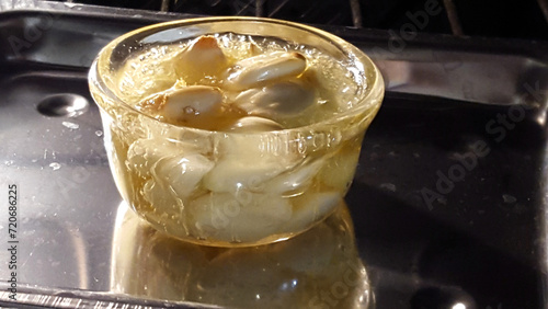 Garlic cloves in boiling olive oil - glass cup in oven