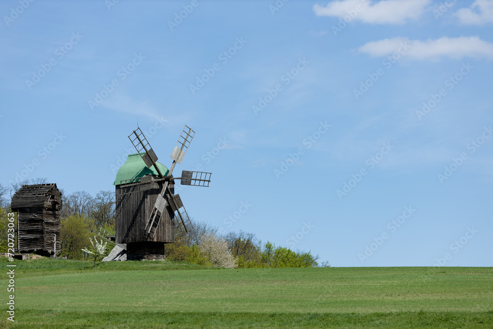 Fototapeta premium Rustic Windmill Amidst Green Fields Under Blue Sky