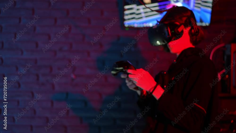 A teenager plays a boxing simulator, standing in a VR club, wearing VR glasses and with controllers in his hands. A young man in a dark room with red backlight A teenager plays a boxing simulator, standing in a VR club, wearing VR glasses and with controllers in his hands. A young man in a dark room with red backlight