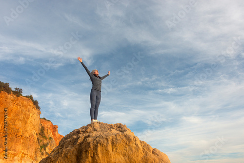 woman with her arms raised after climbing up a rock and standing at the summit