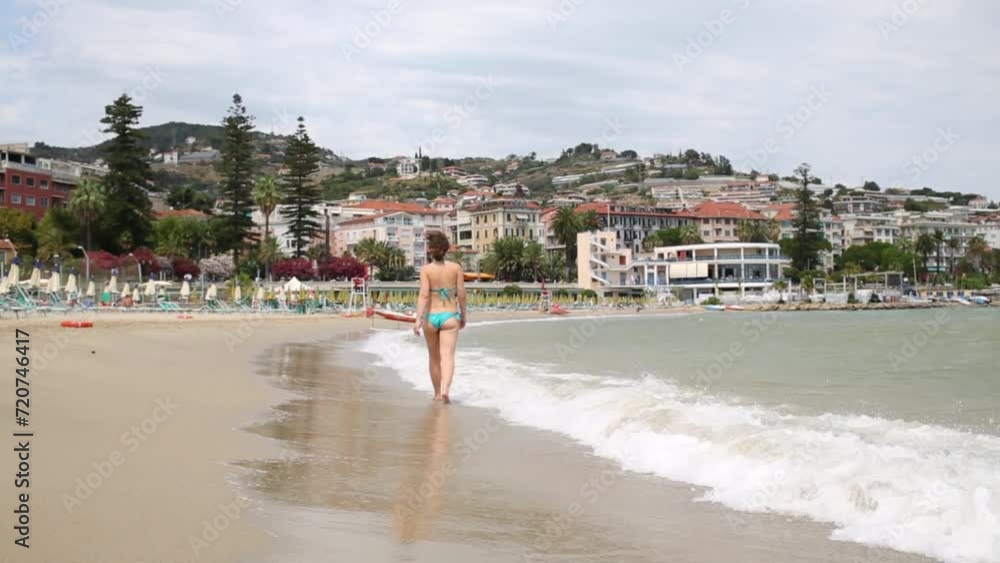 Woman in a blue bathing suit goes away on the beach Woman in a blue bathing suit goes away on the beach