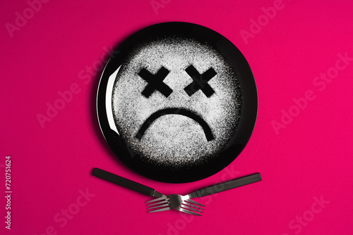 Sad face, concept made with plate and flour, majenta background, x-shaped eyes, black plate, happy mood, facial expressions, forks in the shape of arms with different positions