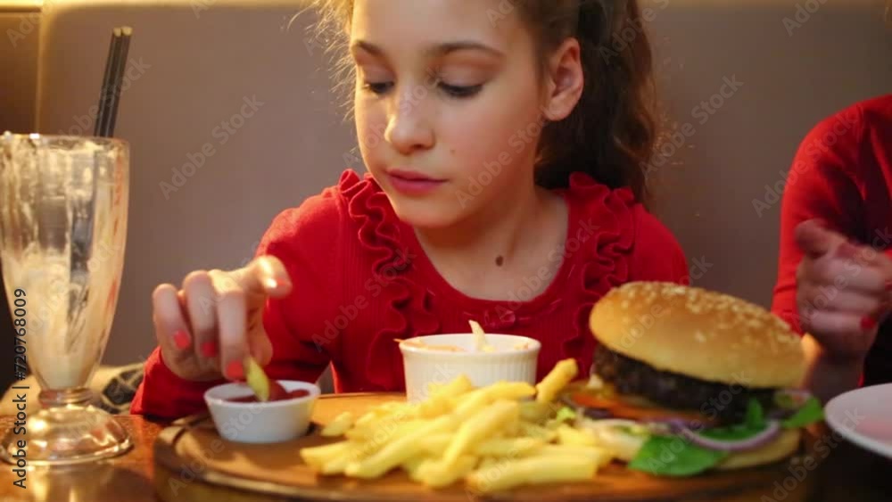 Girl eats french fries at table with hamburger in restaurant Girl eats french fries at table with hamburger in restaurant