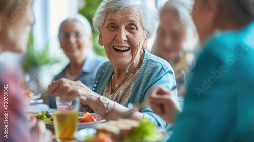 Group of senior friends communicating while eating lunch in nursing home. Focus is on happy woman.