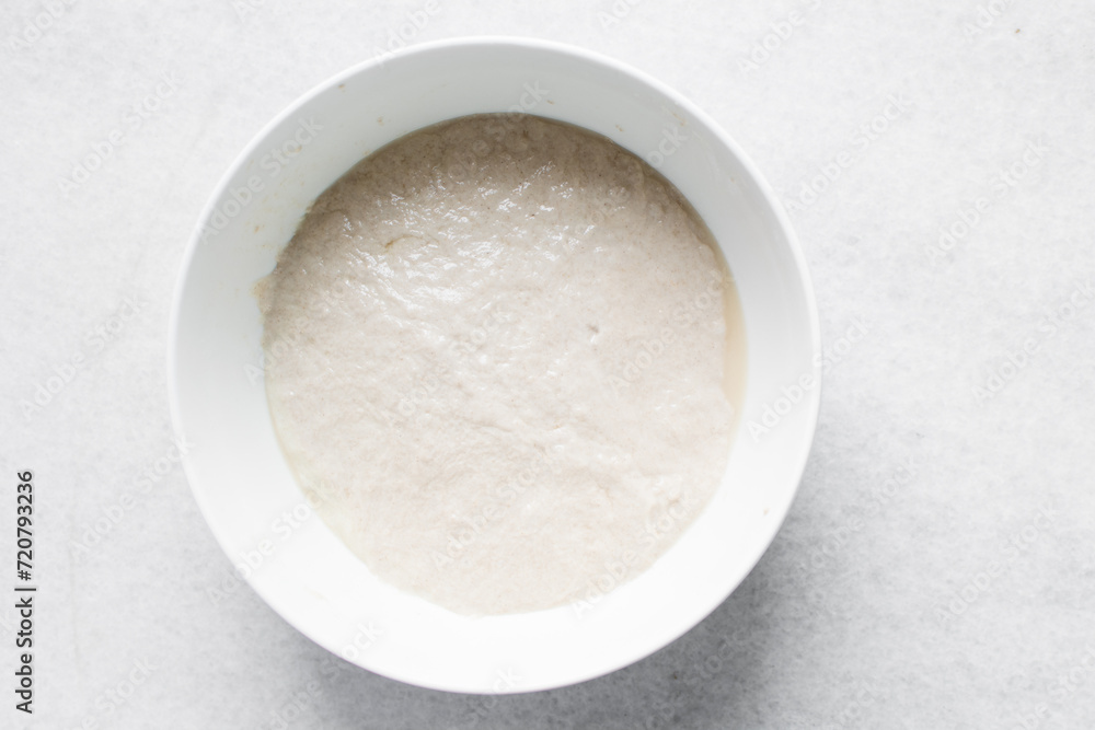 High hydration bread dough resting in a white bowl, Top view of wet