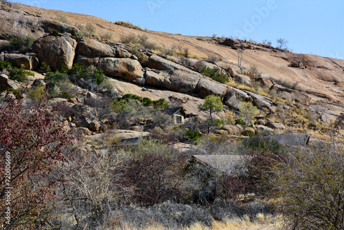 A house has been built behind the dry trees and bushes under a rocky mountain. A good place for seclusion and relaxation