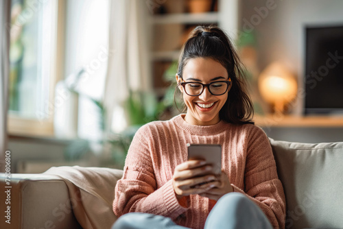 Young adult woman using online mobile bank in her living room, smiling. She is testing a new banking application and is therefore paid. photo