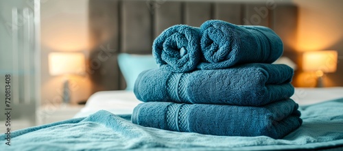 A cozy indoor scene featuring a neatly stacked tower of blue towels against a textured wall, adding a touch of comfort and warmth to the inviting bed adorned with a soft blanket photo