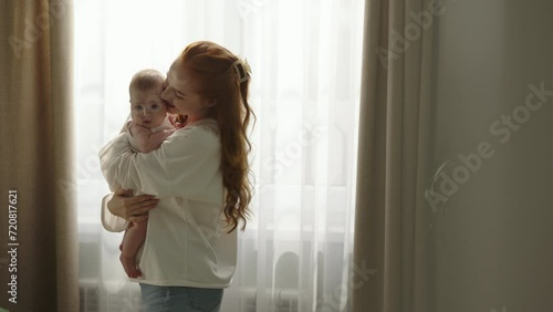 Woman mother hugging baby lovingly softly. Young mother smiles, laughs, holds beloved dear child in arms, swaying from side to side. Concept of happy motherhood, parenthood. Child in arms of mommy.