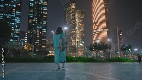 Woman citizen with backpack returns home on street in megapolis at night. photo