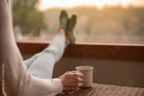 woman at home enjoying the sunrise from window and a cup of warm cup of coffee 