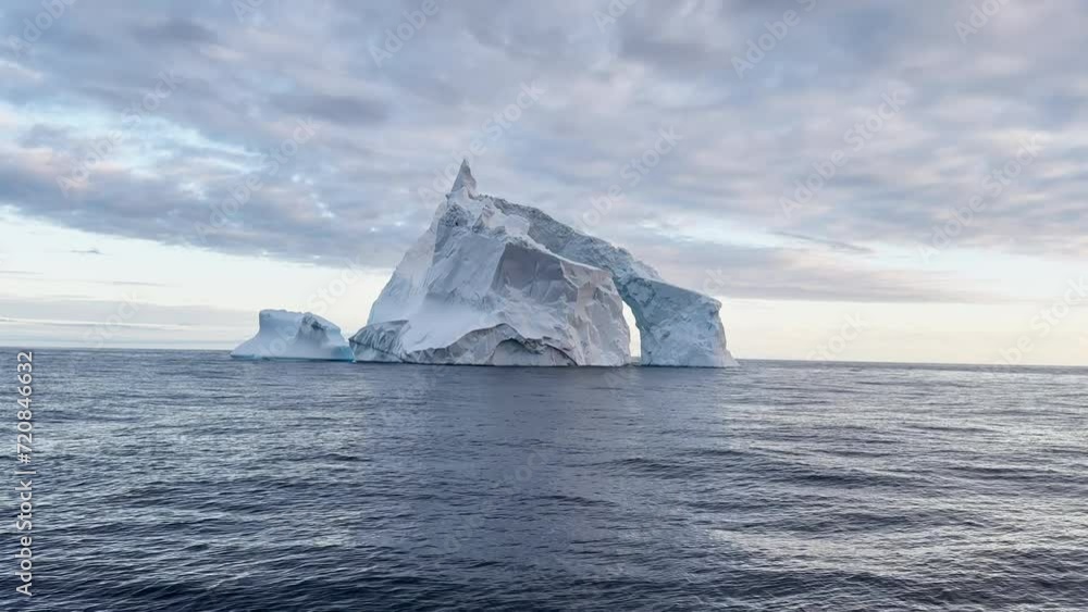 Arch in a huge iceberg, high breakaway glacier drifts in the southern ocean off the coast of Antarctica at sunset, the Antarctic Peninsula, the Southern Arctic Circle, azure water, cloudy weather Arch in a huge iceberg, high breakaway glacier drifts in the southern ocean off the coast of Antarctica at sunset, the Antarctic Peninsula, the Southern Arctic Circle, azure water, cloudy weather