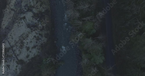 Ungraded high angle aerial drone footage of an isolated road in a forest alongside a river on an early sunny morning in Washington State.