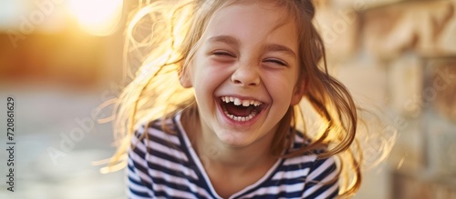 Young Girl in Striped Shirt Bursting with Laughter as She Poses Playfully © AkuAku