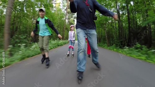 Man, woman and two children roller skate in green park, man makes selfie photo