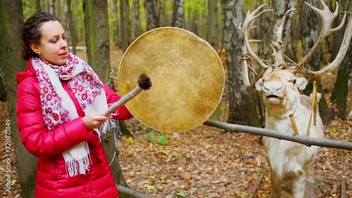 Woman beats tambourine near stuffed deer in forest at autumn day photo