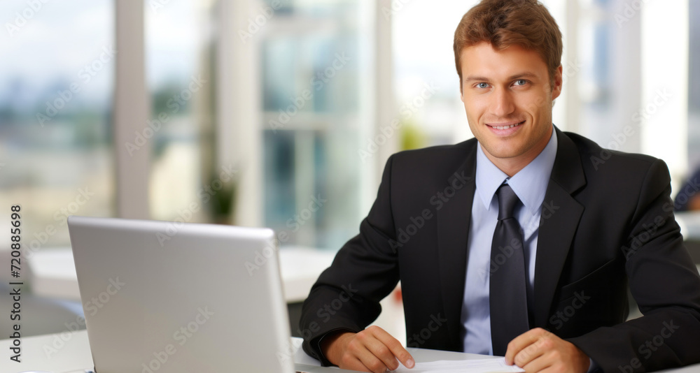 Handsome businessman sitting at desk in office and working on laptop Handsome businessman sitting at desk in office and working on laptop