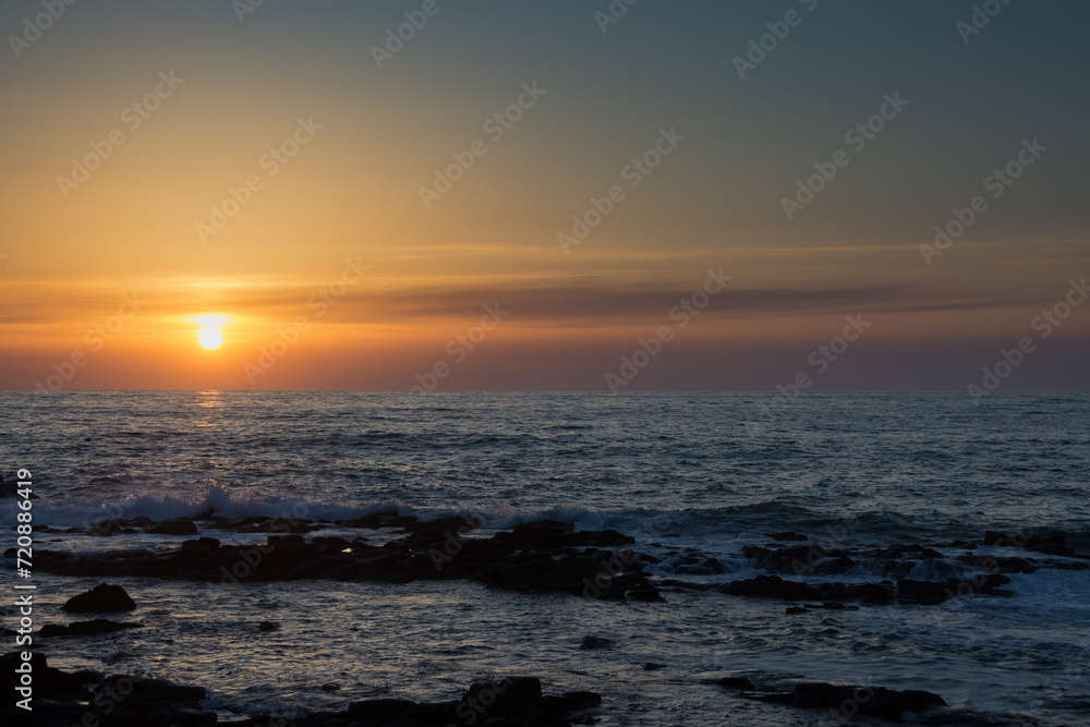 水平線に沈む夕陽と岩の海岸
