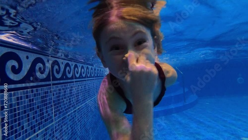 Cute little girl dives in the pool holding her nose. Family moments, joy, swimming pool. 