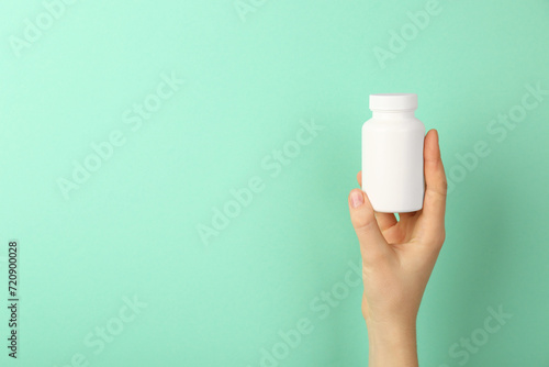 Woman holding blank white jar of vitamins on turquoise background, closeup. Space for text