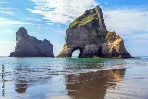 Rock formations reflect in the water at Wharariki Beach, New Zealand