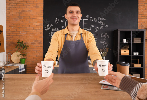 Male barista giving coffee cups to visitors in cafe