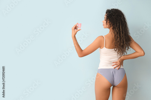 Young woman in menstrual panties on blue background, back view photo