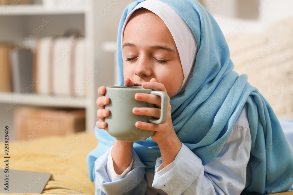 Little Muslim girl in hijab drinking tea while lying on bed at home Little Muslim girl in hijab drinking tea while lying on bed at home